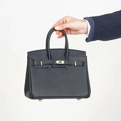Hand holding a black handbag with gold hardware on a white background