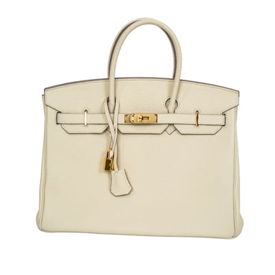 Beige handbag with gold hardware on a light gray background