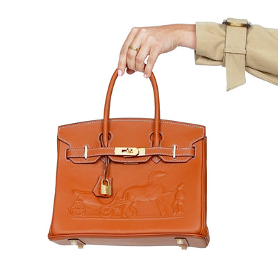 Orange handbag with gold hardware held by a hand against a white background